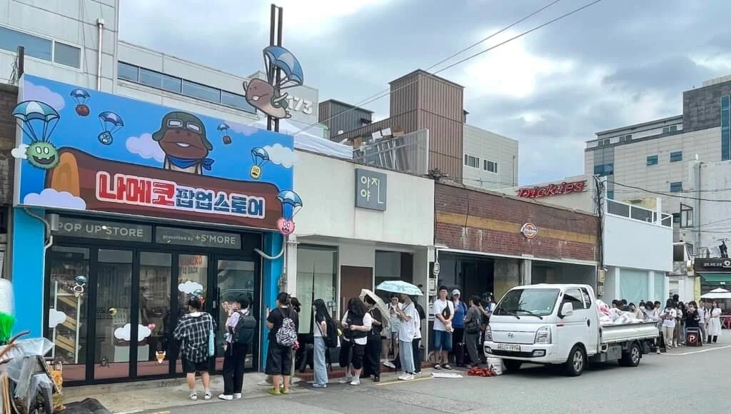 韓国の街角に立つ「ナメコ 팝업스토어」（ナメコ ポップアップストア）の前で、多くの若者たちが長蛇の列を作っています。