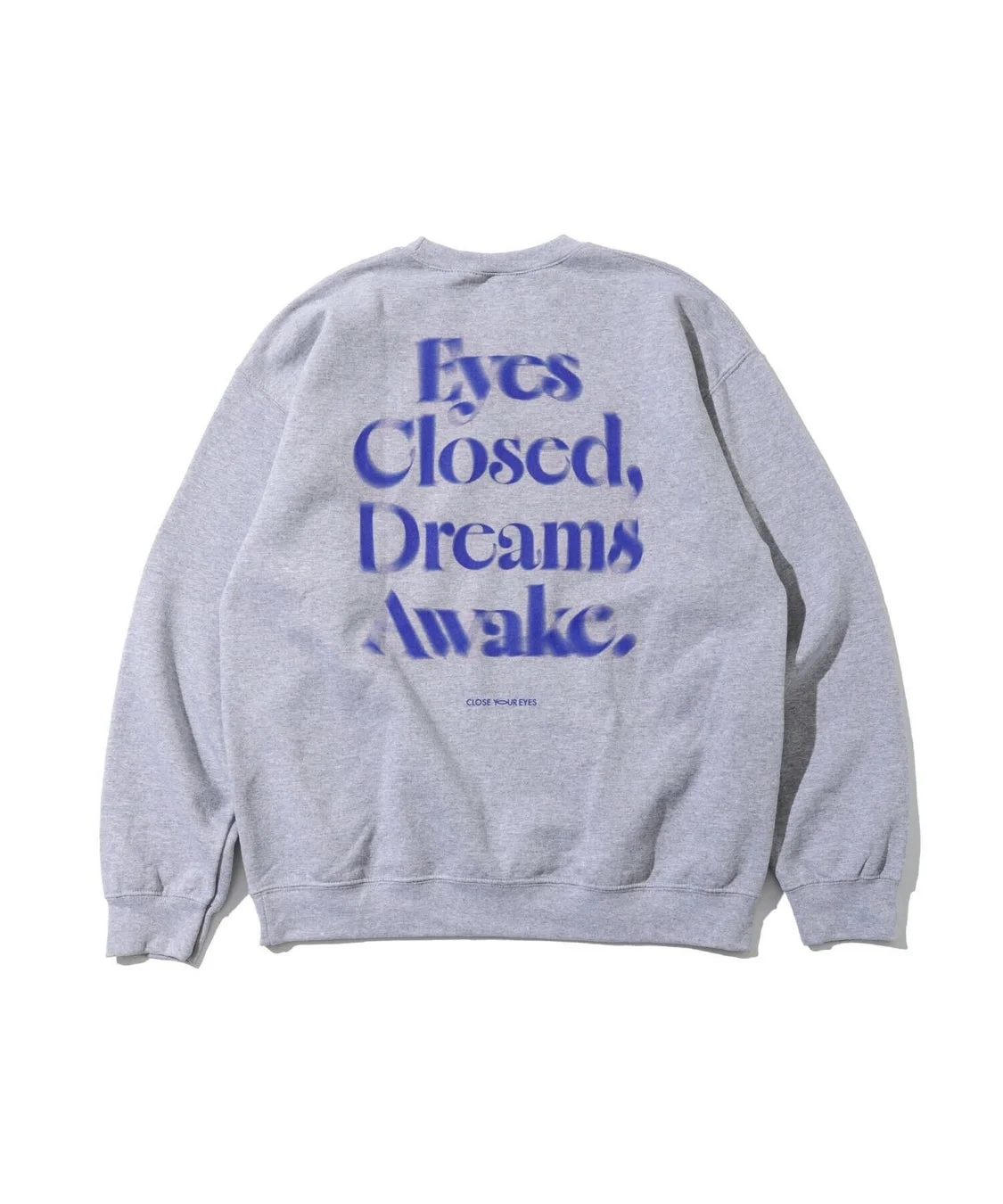 灰色のスウェットシャツの背面が写っており、「Eyes Closed, Dreams Awake.」という青色の文字が大きくプリントされています。その下には「CLOSE YOUR EYES」と小さく書かれています。シンプルでカジュアルなファッションアイテムです。