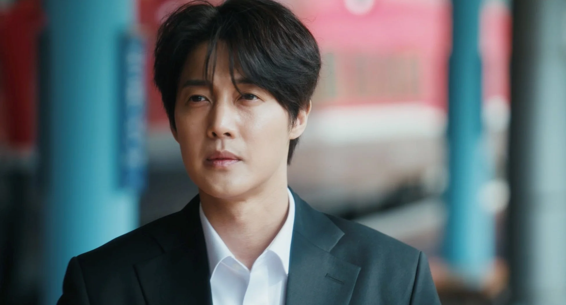 黒いスーツと白いシャツを着用した男性のポートレート。真剣な表情を浮かべ、カメラを見つめています。