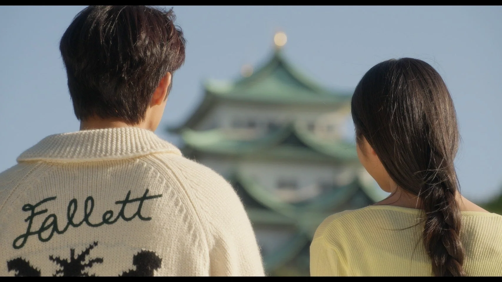 名古屋城らしき日本の城を背景に、後ろ姿の男女が並んで景色を眺めている様子。