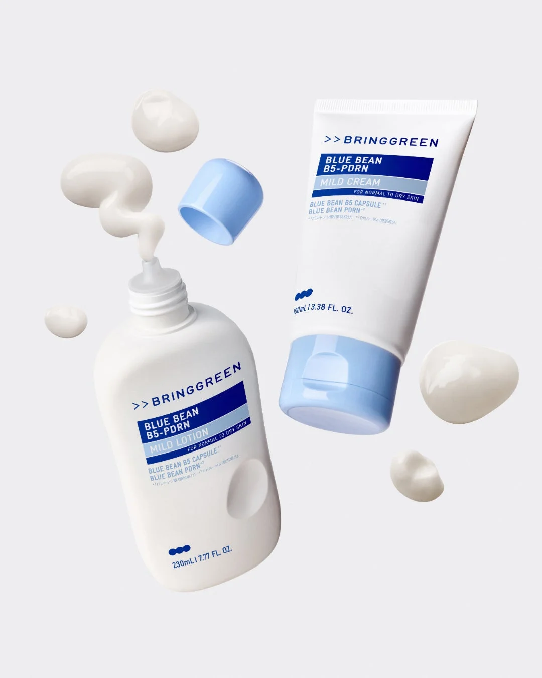 白を基調とした背景に、BRINGGREENの「BLUE BEAN B5-PDRN」シリーズのマイルドローションとマイルドクリームが配置されています。製品の一部が飛び散り、そのテクスチャーが表現されており、乾燥肌向けのスキンケア製品であることが伝わる写真です。