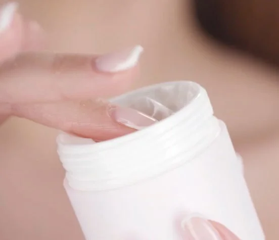 白い容器に入ったクリーム状の製品に触れる女性の指
