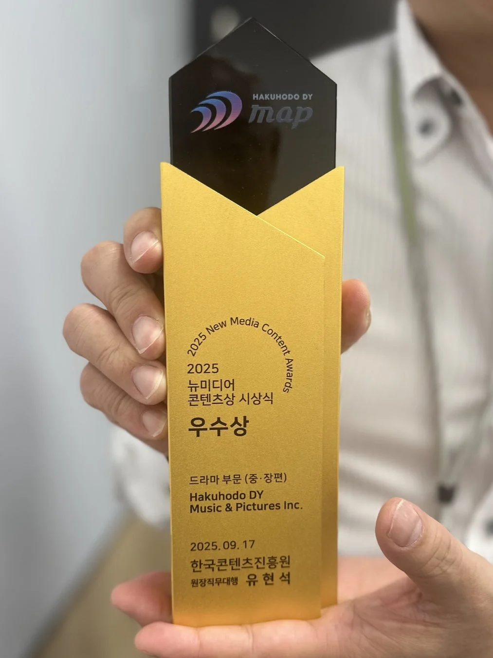 2025年ニューメディアコンテンツアワードで「優秀賞」を受賞したトロフィーを手に持っている画像