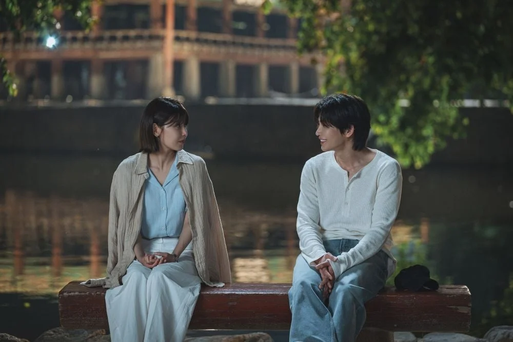 夜の水辺のベンチに座る男女が笑顔で会話している