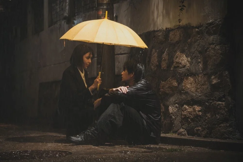 雨の夜の路地で傘を差して座り込む男女