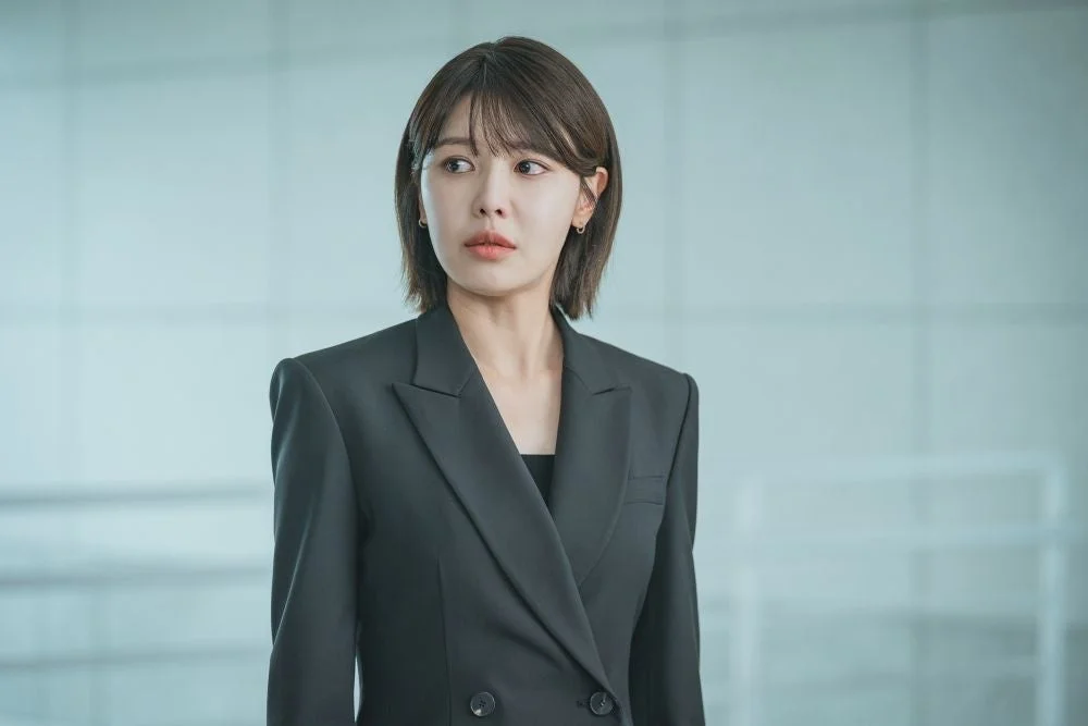 黒いスーツを着用し真剣な表情を浮かべるショートヘアの女性