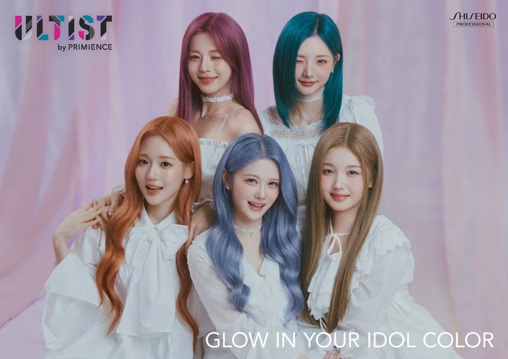 5人の女性がそれぞれ異なる鮮やかなヘアカラーと白い衣装をまとい、笑顔でポーズ