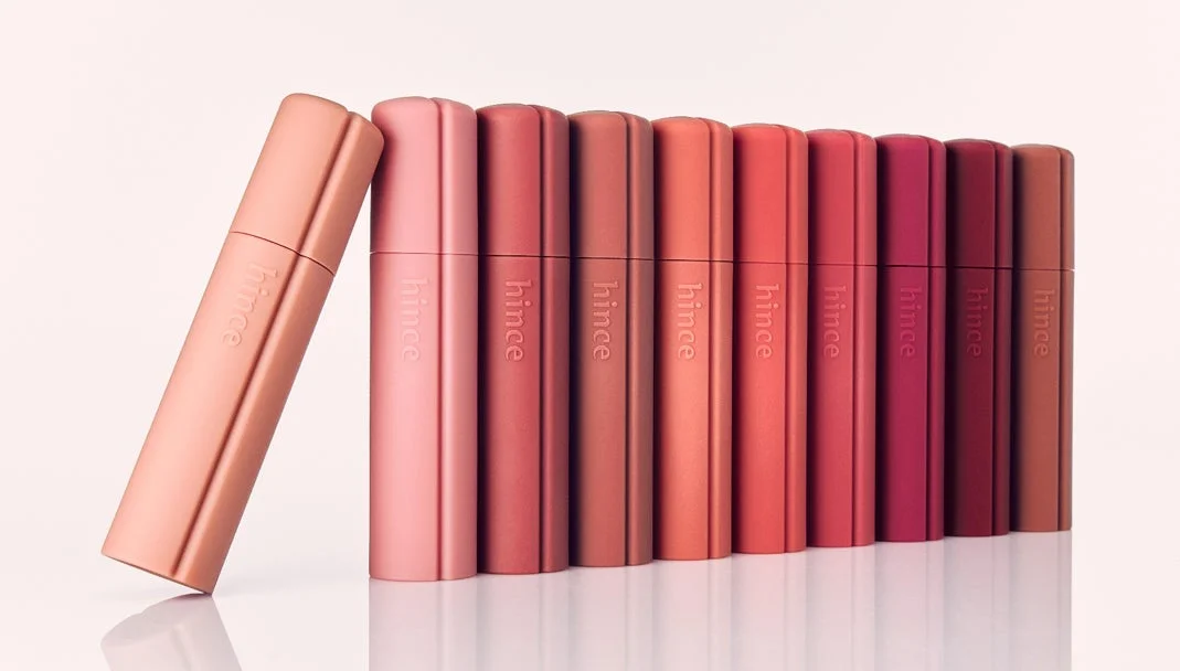 hinceのリップスティックが、ピンクからレッド系のグラデーションで複数本並べられています。一本は斜めに立てかけられており、様々な色合いが表現された美しい商品写真です。