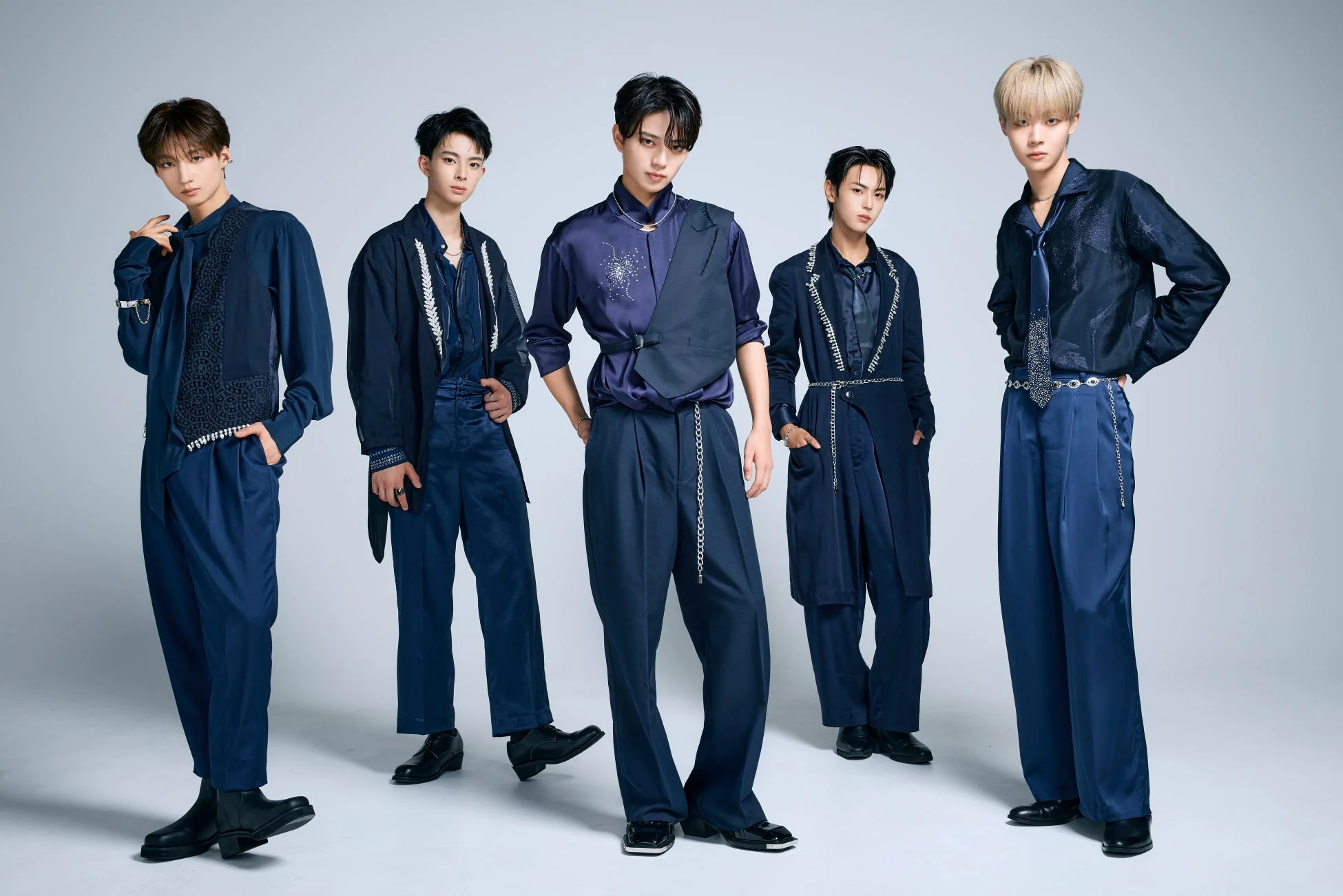 ネイビーの衣装をまとった5人の若い男性アイドルグループが、白い背景の前でポーズをとっているスタジオ写真
