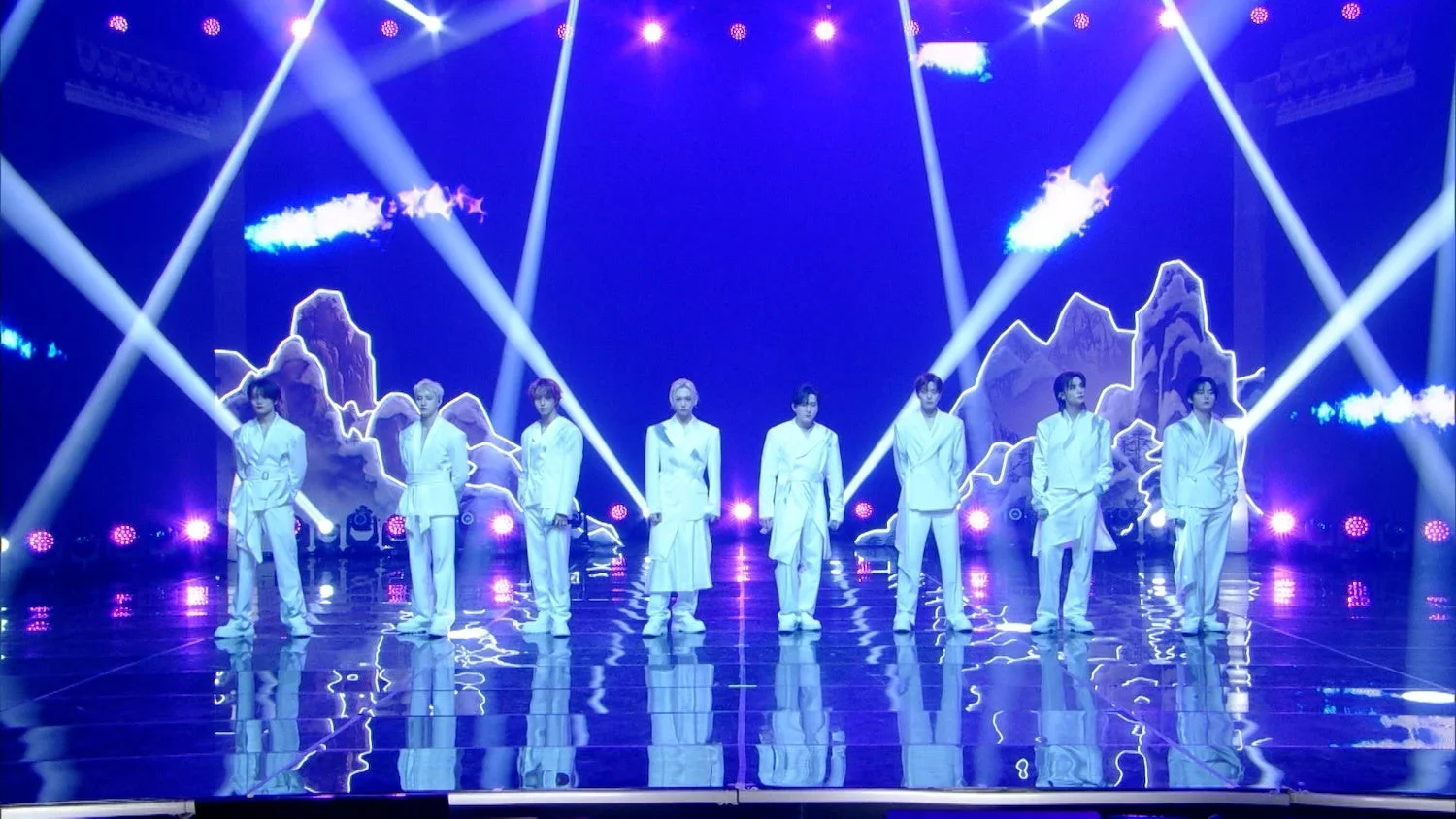 青い光の中で白い衣装の9人組男性グループがパフォーマンス