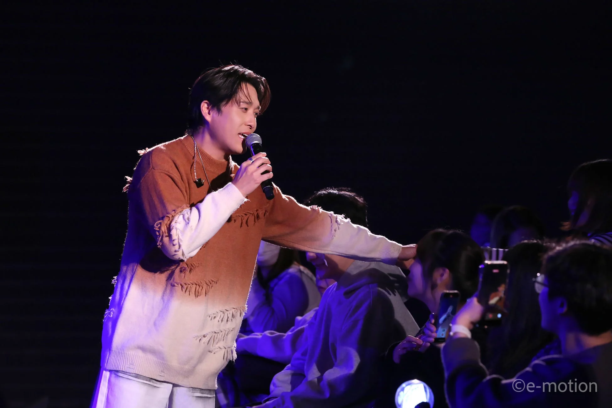 ステージ上でマイクを持って歌う男性アーティストが、観客と交流している様子を捉えた写真です。