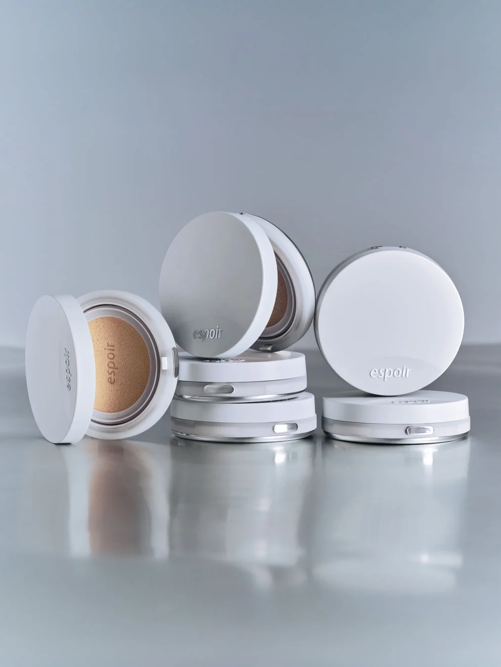 白いコンパクト型化粧品「espoir」が複数配置されたスタジオ撮影の写真です。一部は開いており、クッションファンデーションのような中身が見えます。