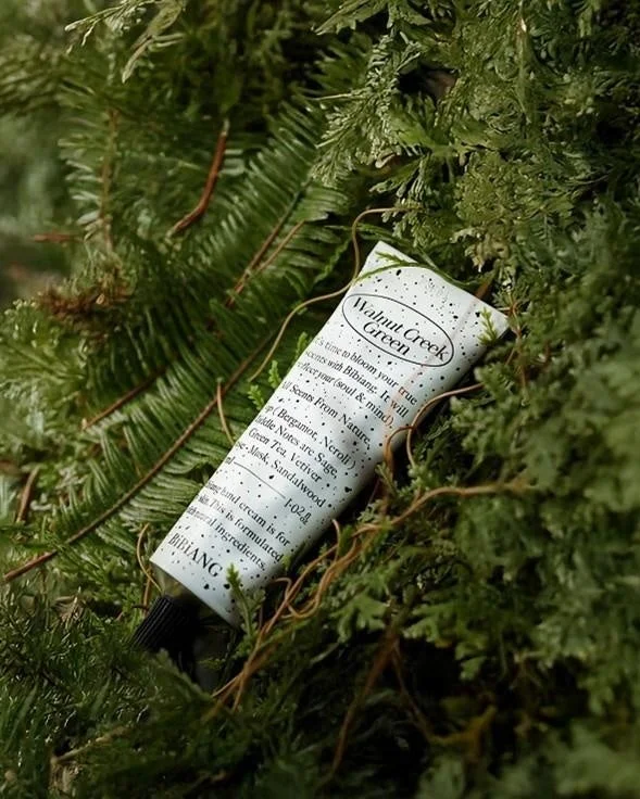 緑豊かな植物の中に置かれた、「Walnut Creek Green」という名前のBIBIANG製ハンドクリームのチューブ