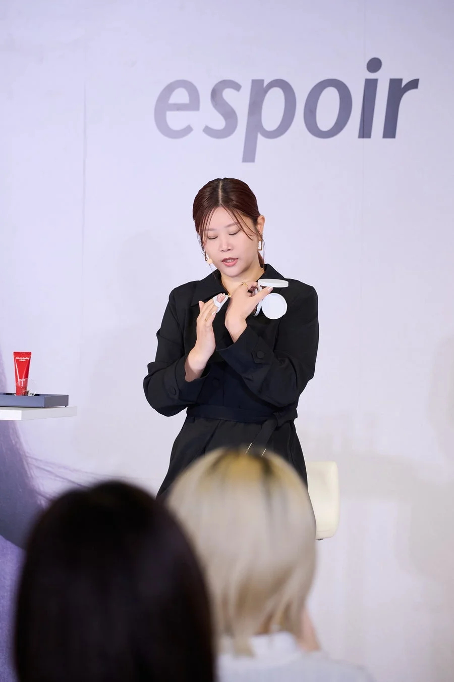 美容イベントで、女性がespoirのクッションファンデーションとパフを使って実演している様子です。背景にはブランドロゴが見えます。