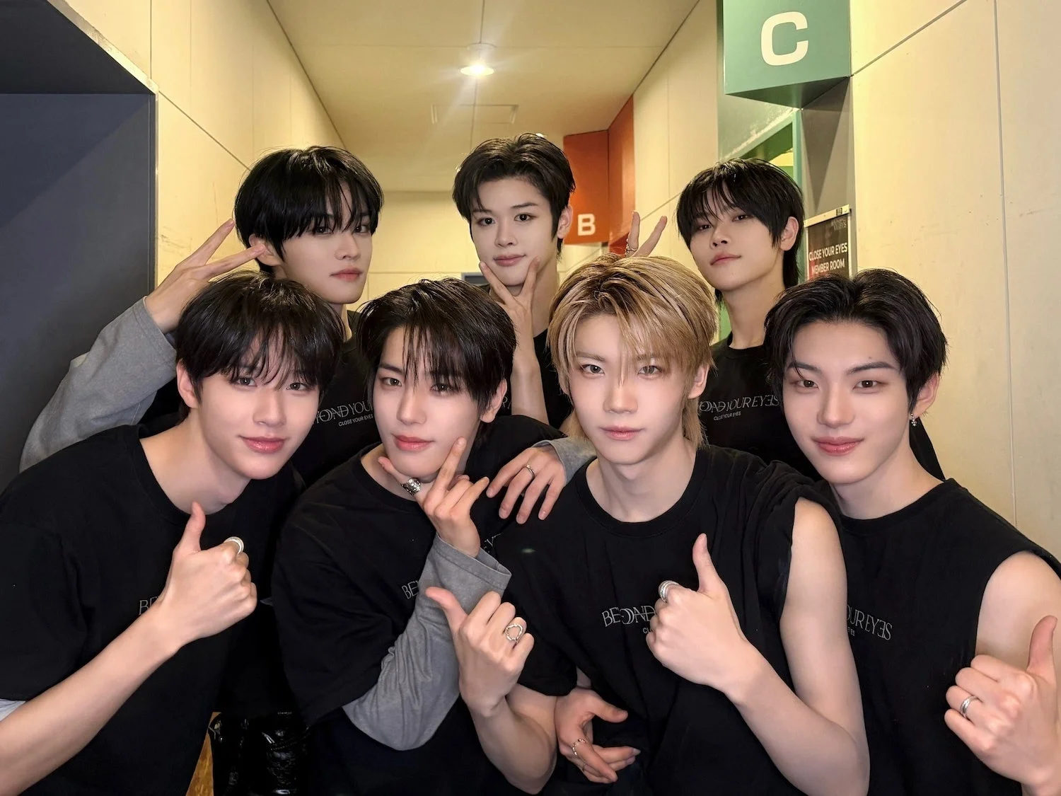 7人の若い男性アイドルグループのメンバーが、黒いTシャツを着て笑顔でポーズをとっている集合写真