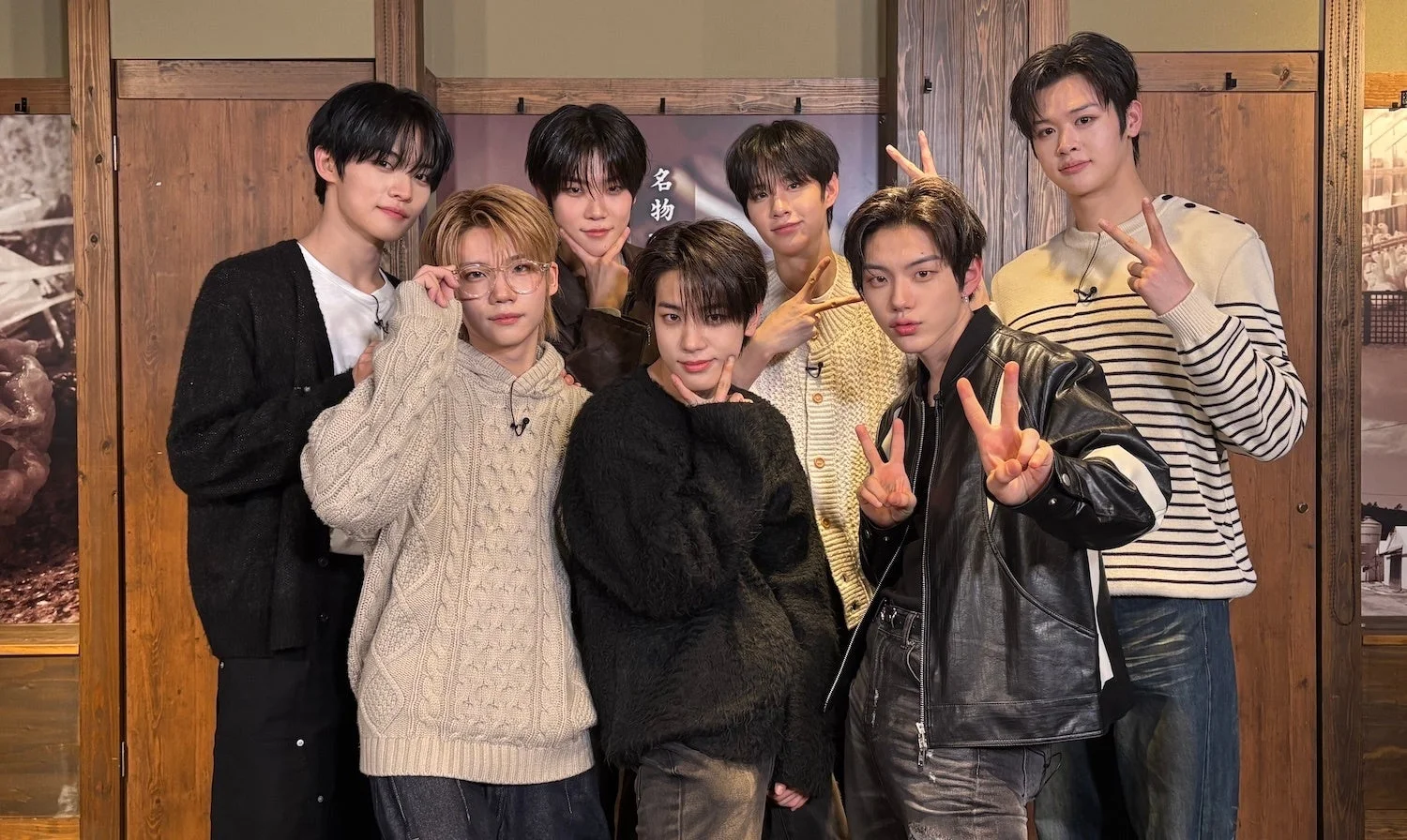 木目調の壁を背景に、7人の若い男性が様々なポーズで写っている集合写真