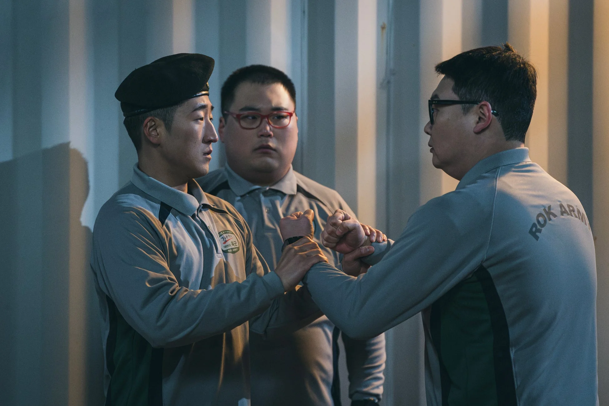 軍服のような服装の3人の男性が写っており、手前の2人が互いの腕を掴み合っている