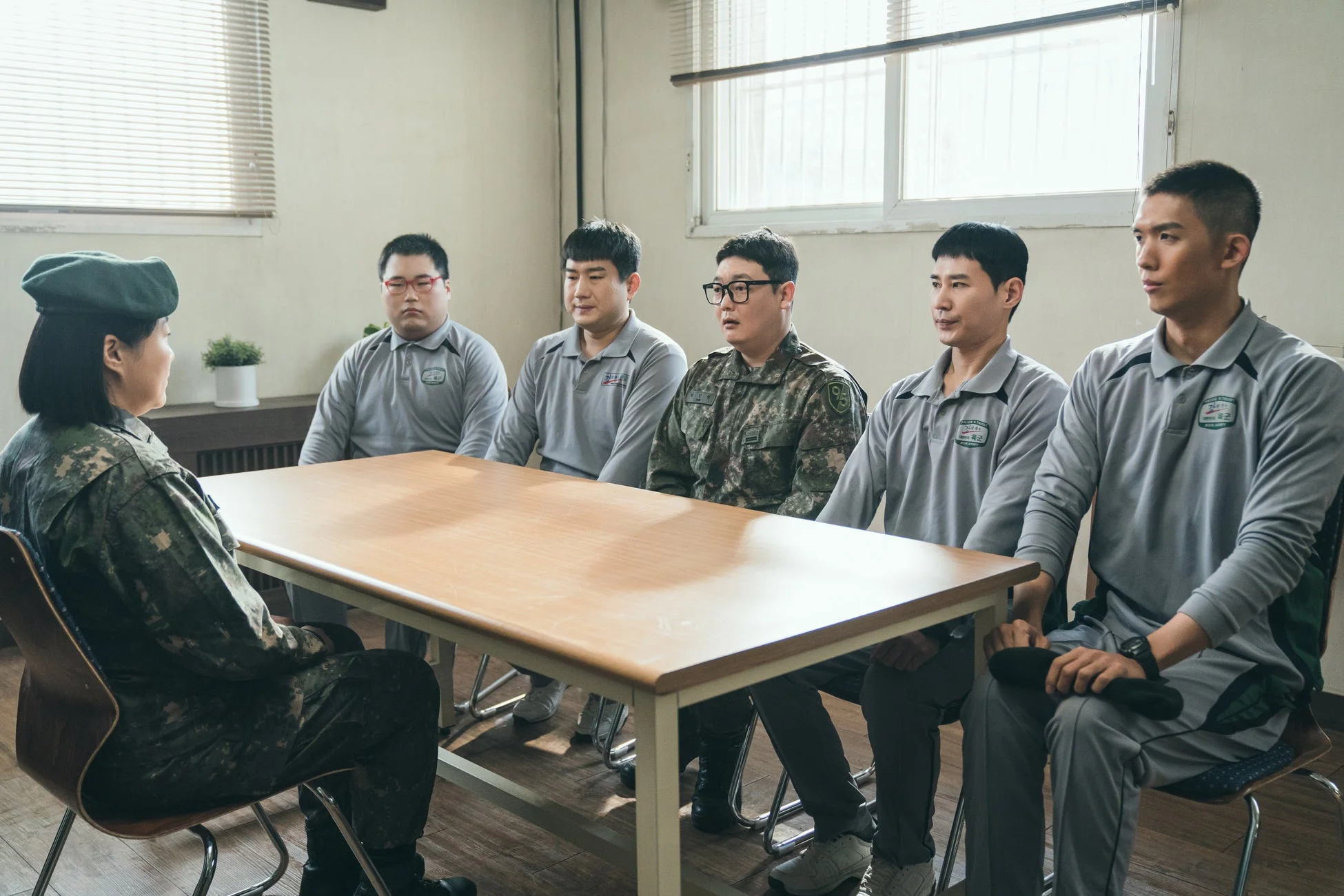 軍服姿の女性将校と、グレーのポロシャツを着た兵士、迷彩服の兵士がテーブルを囲んで座っている