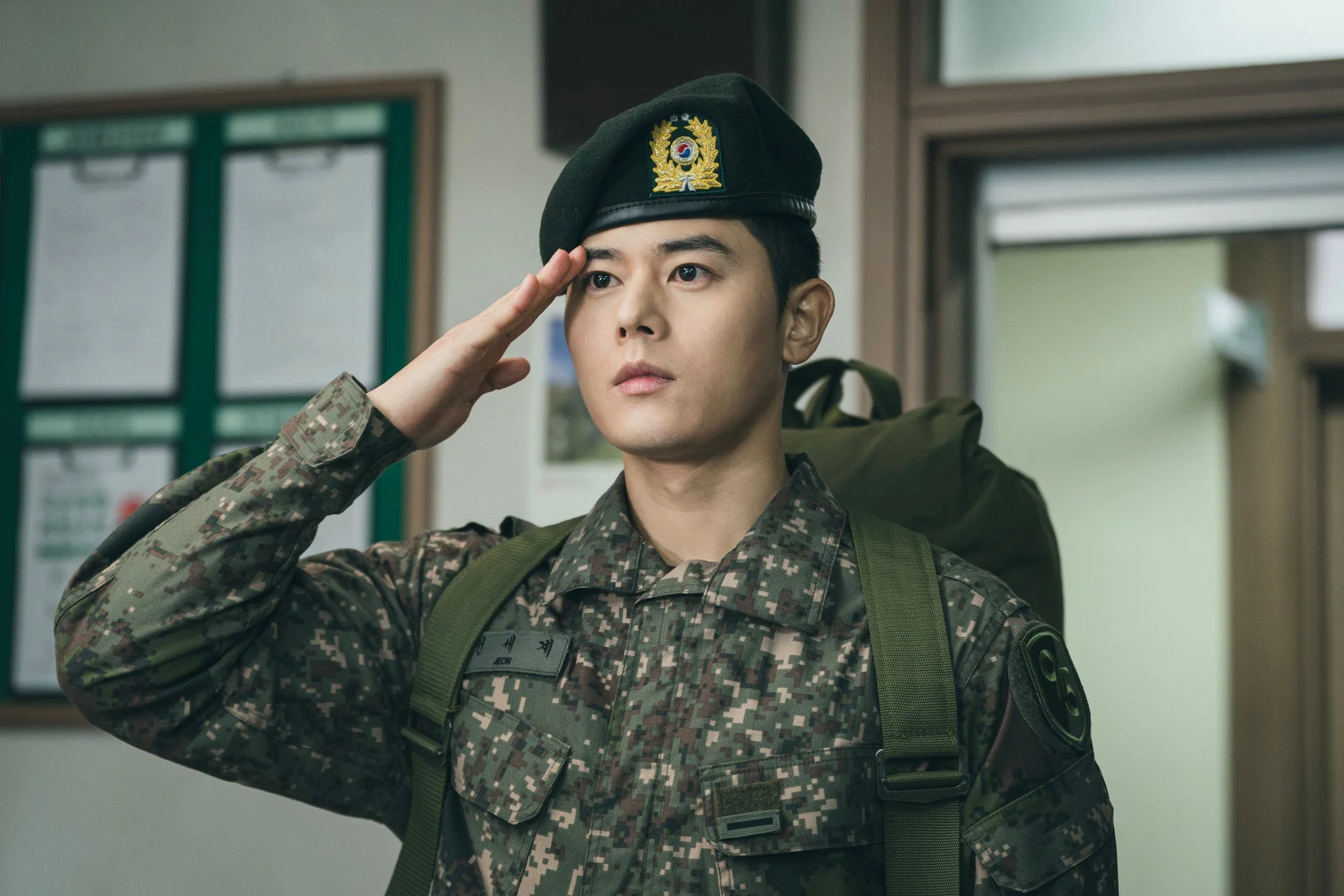 韓国軍の迷彩服とベレー帽を着用した男性が、室内で真剣な表情で敬礼をしている