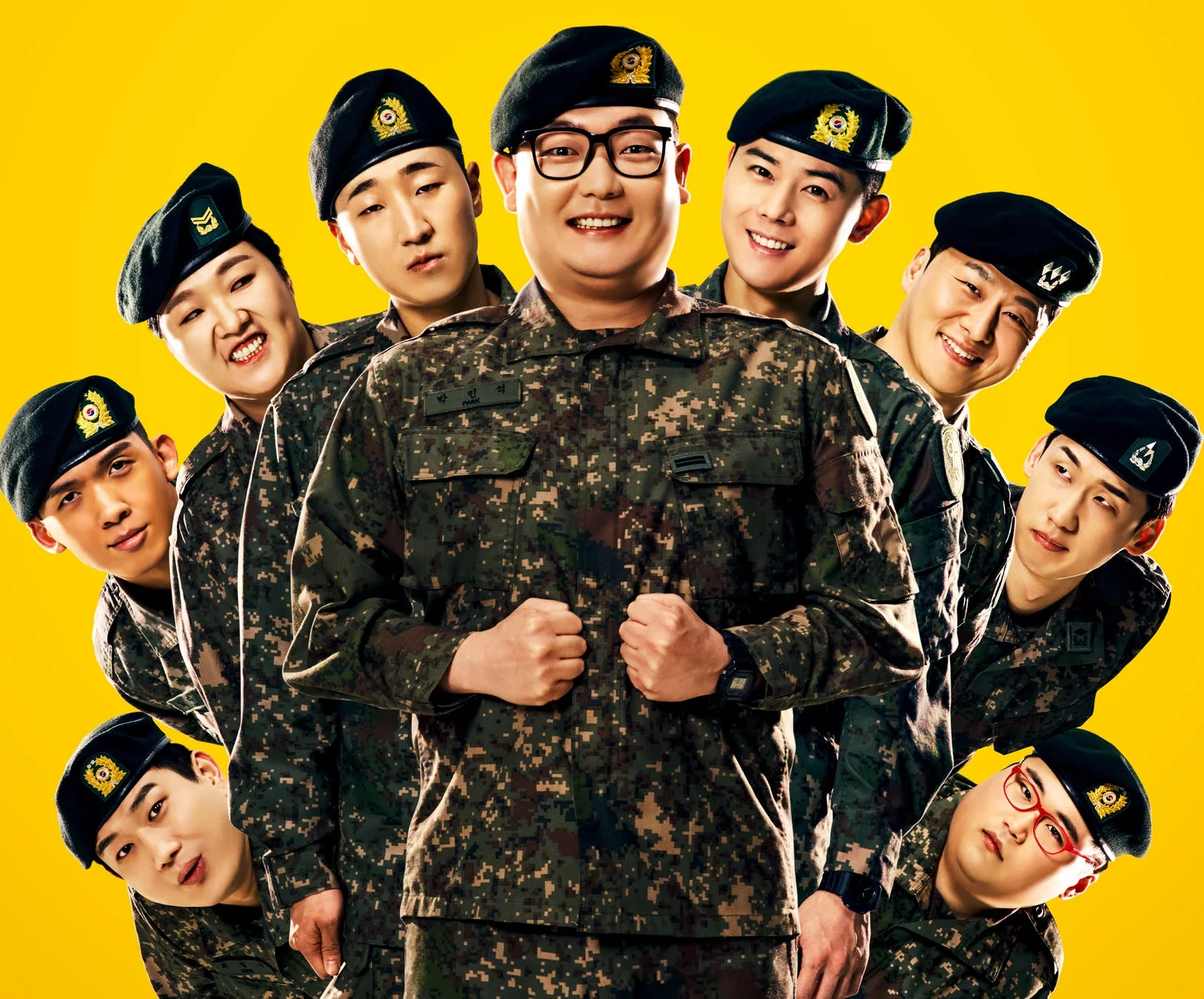黄色の背景を背に、迷彩服と黒いベレー帽を着用した8人の男性
